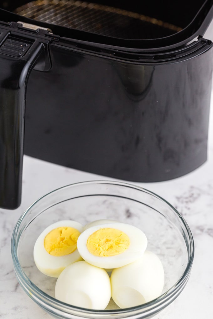 freshly cooked and halved air fryer hard boiled eggs placed in a clear glass bowl with the air fryer machine in the background