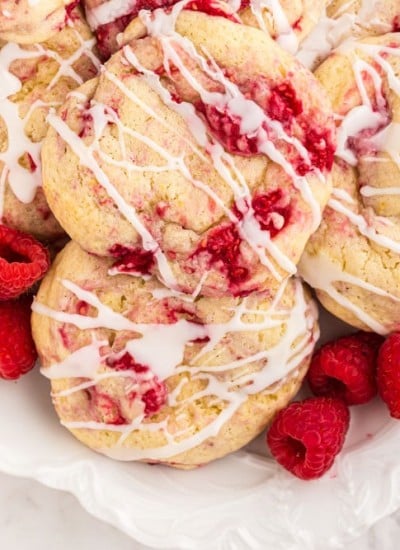 baked lemon raspberries cookies served on a white tray with fresh raspberries scattered around as garnish
