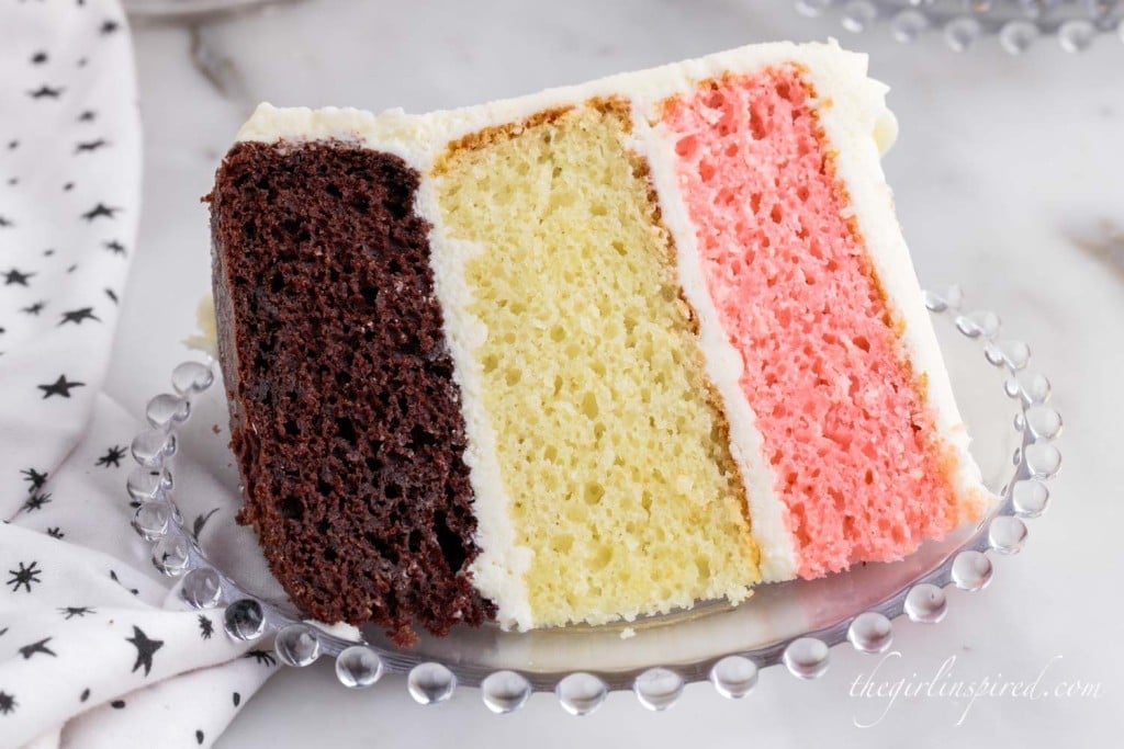 a slice of neapolitan cake with three layers on a small glass plate