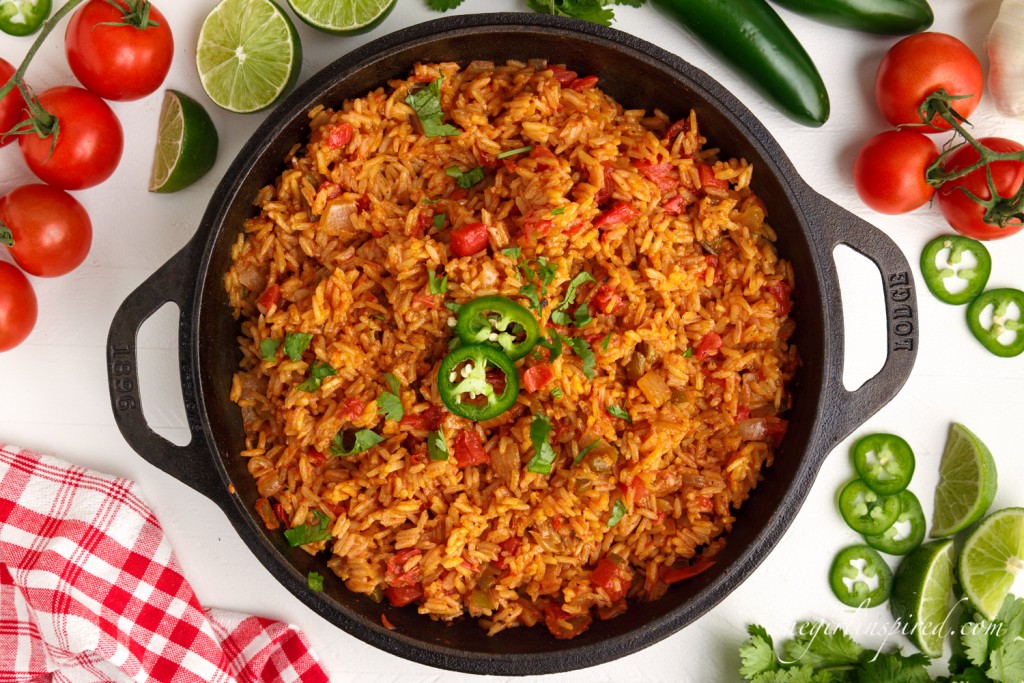 top view of mexican rice in a skillet next to other ingredients topped with sliced jalapenos