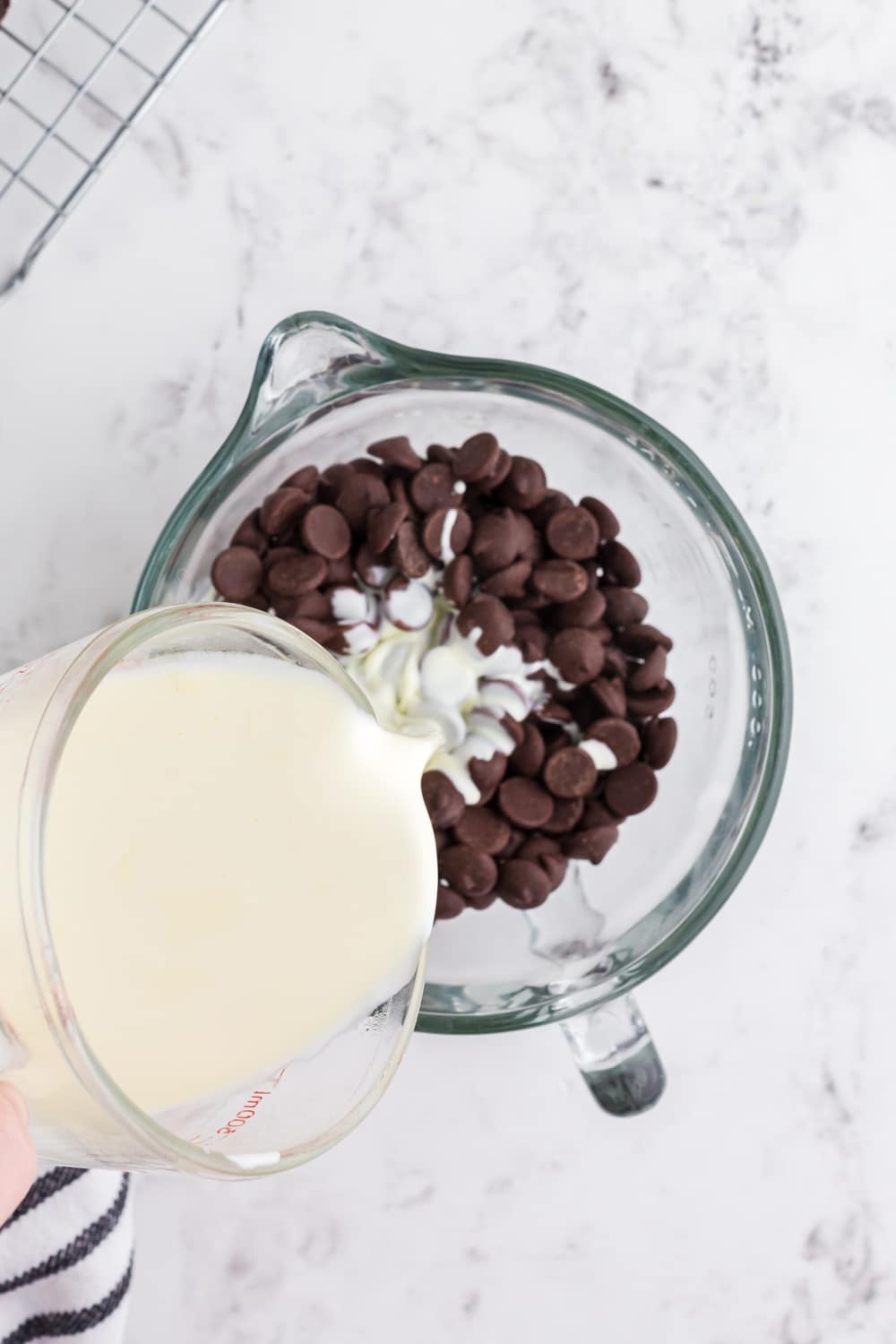 Heavy cream pouring into large glass bowl with chocolate chips.