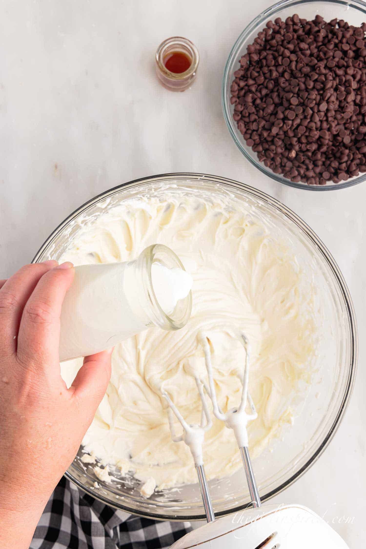 pouring heavy cream from bottle into cream cheese mixture.