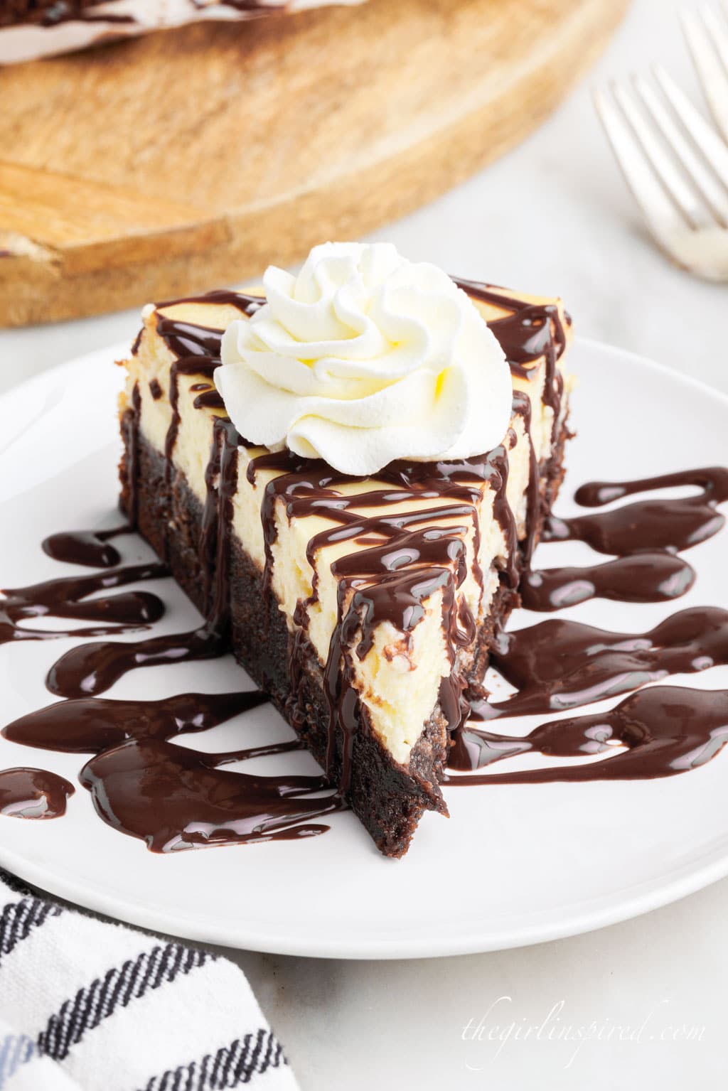 a slice of Brownie Bottom Cheesecake on a small white plate drizzled with chocolate