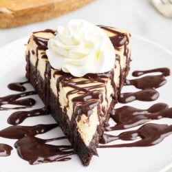 a slice of Brownie Bottom Cheesecake on a small white plate drizzled with chocolate