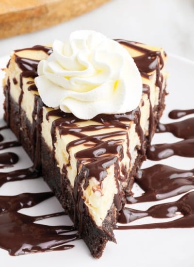 a slice of Brownie Bottom Cheesecake on a small white plate drizzled with chocolate