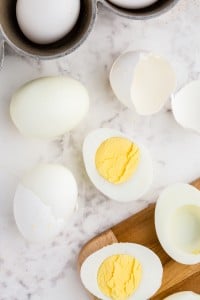 Hard boiled eggs peeled and halved on top of a white marble surface and a section of a wooden board