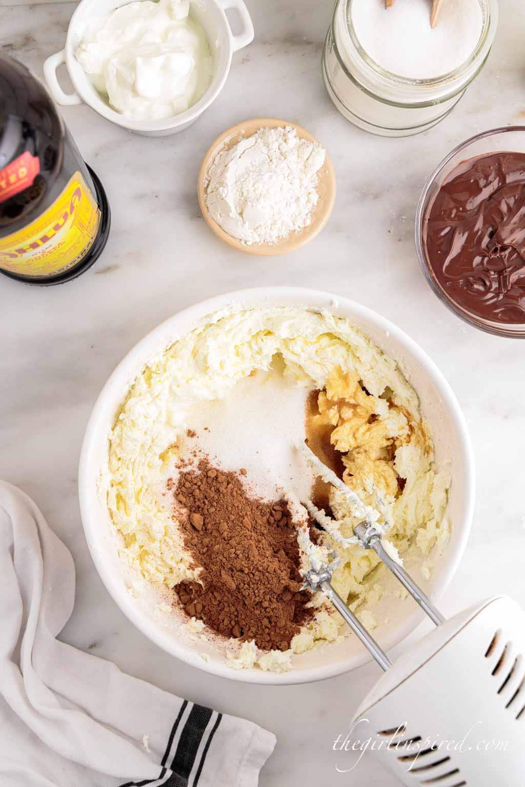 whipped cream cheese in large bowl with cocoa powder, sugar, and vanilla added to bowl.
