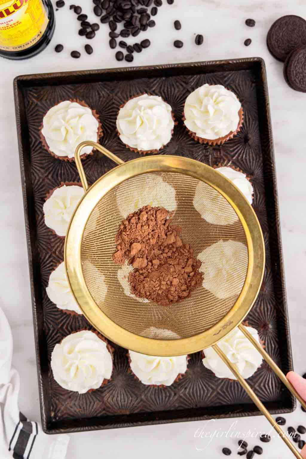 sifter with cocoa powder over cheesecake bites.