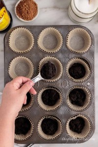 spooning oreo cookie crumbs into lined muffin tin cups.