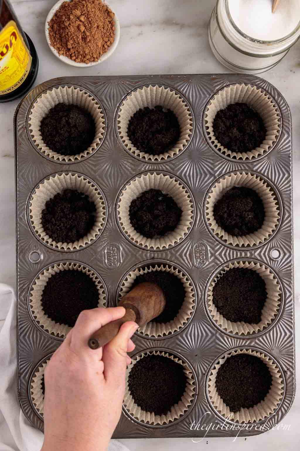 tamping down oreo cookie crumbs in muffin tin cups.