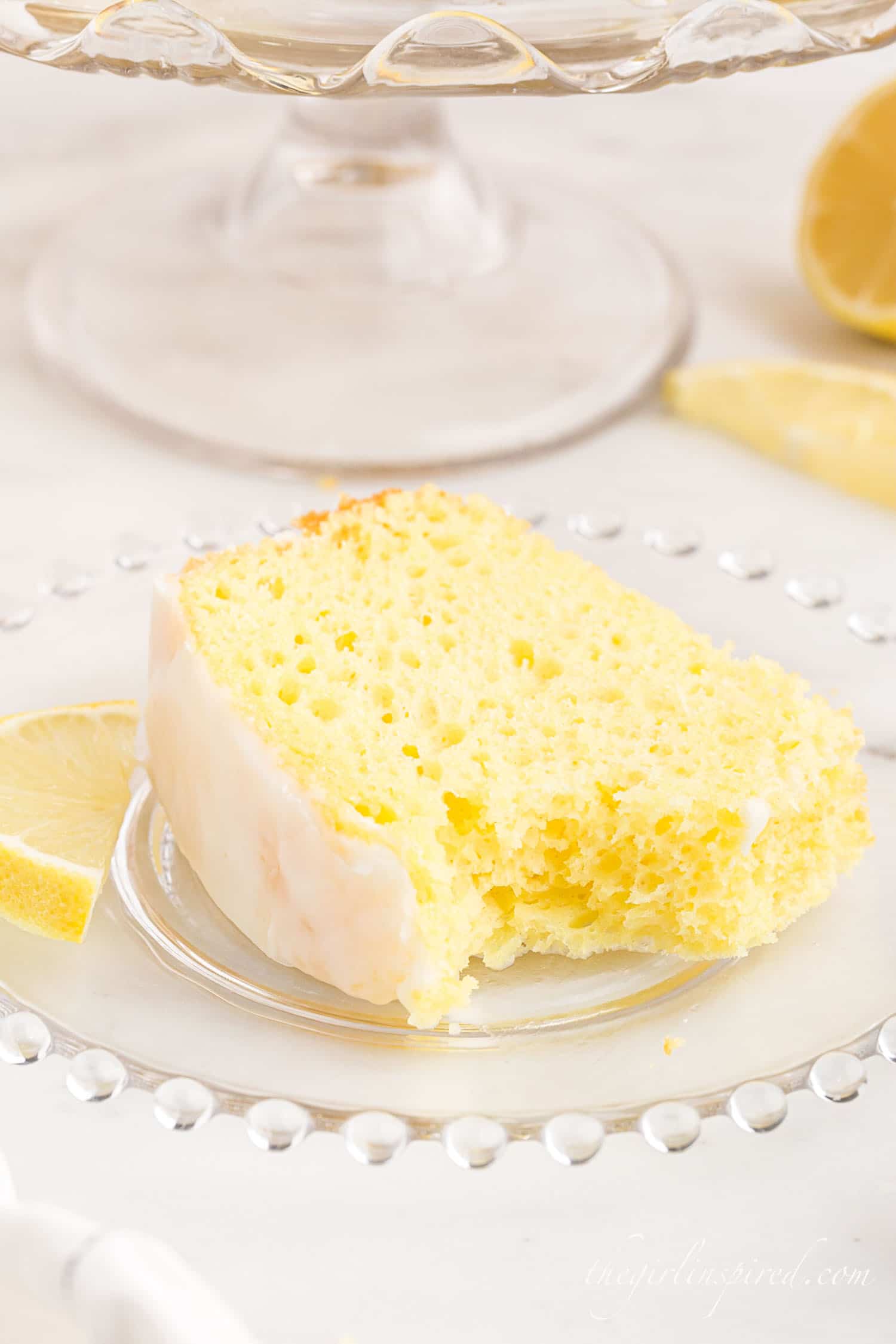 a slice of lemon chiffon cake on a small glass plate with a bite taken out