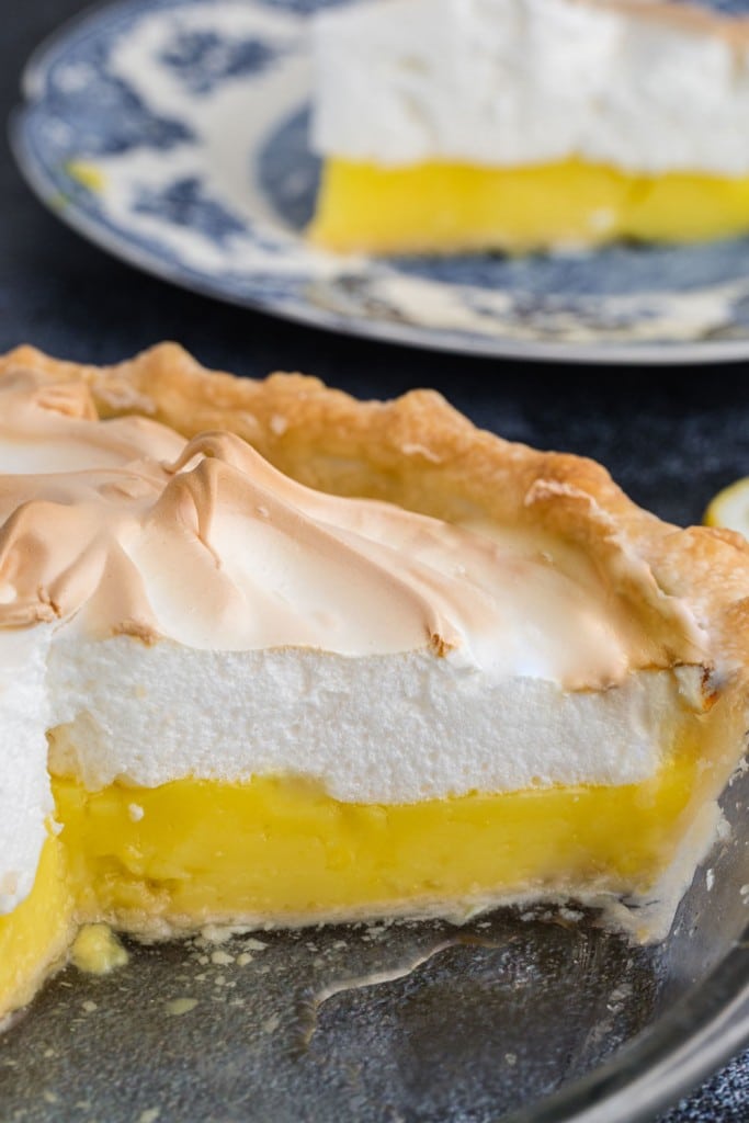 sliced lemon meringue pie with a slice or two removed and a plate holding a slice of pie in the background