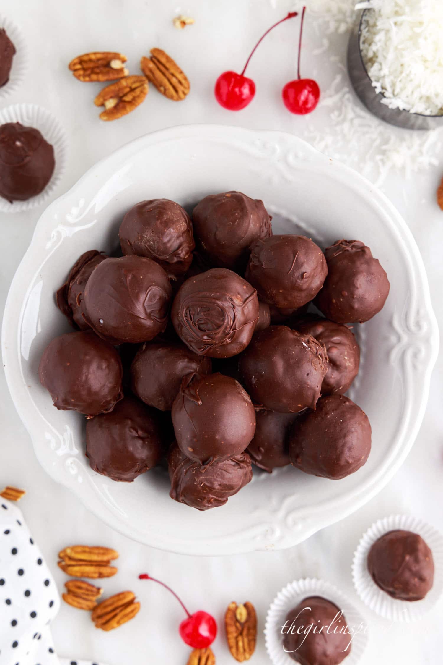 bowl filled with chocolate coated balls, maraschino cherries and pecans scattered about.