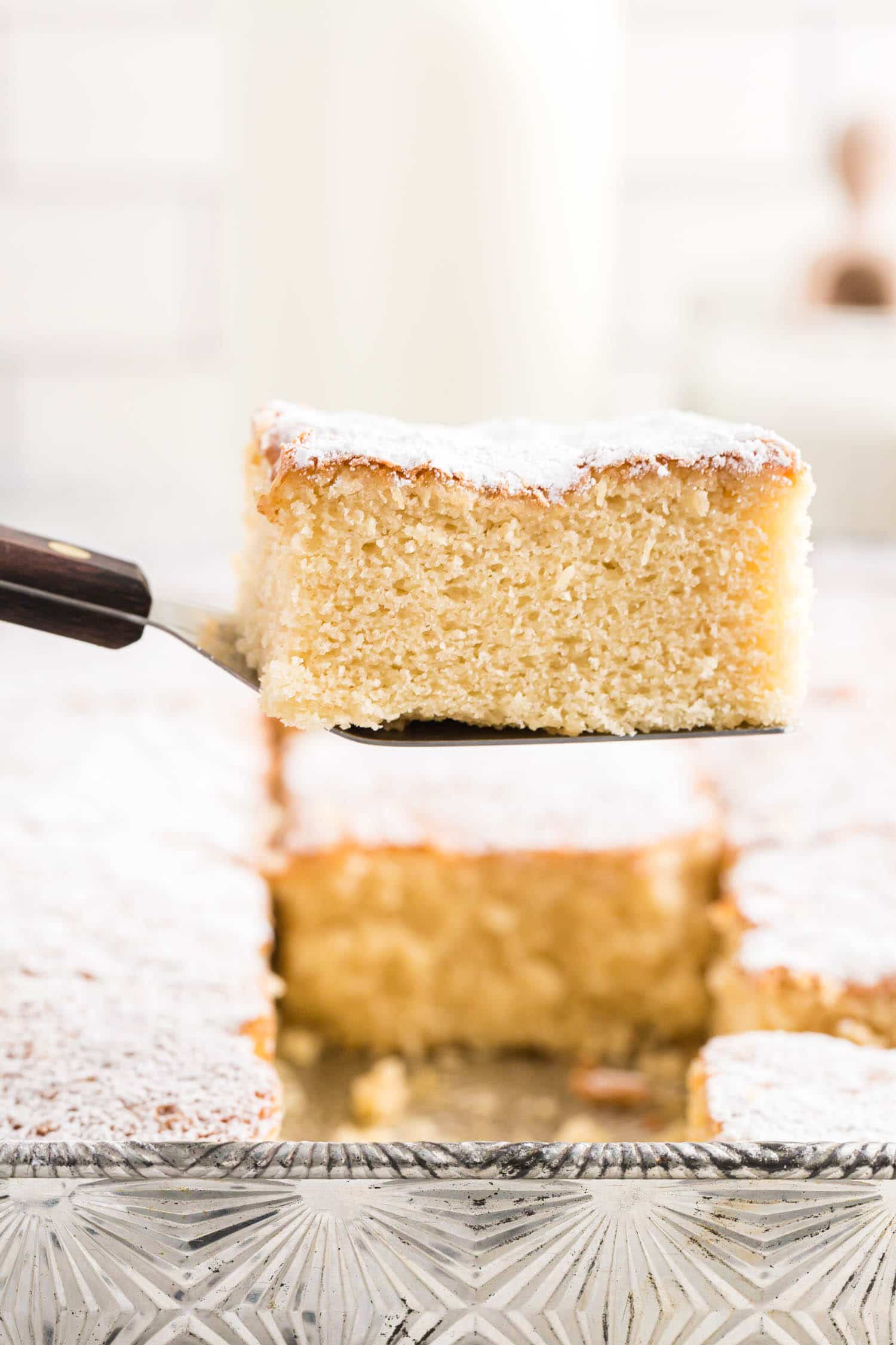 lifting a slice of milk cake out of the pan on a cake server