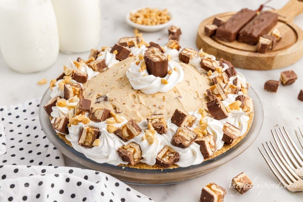 no bake snickers pie topped with peanuts, whipped cream, and chopped snickers