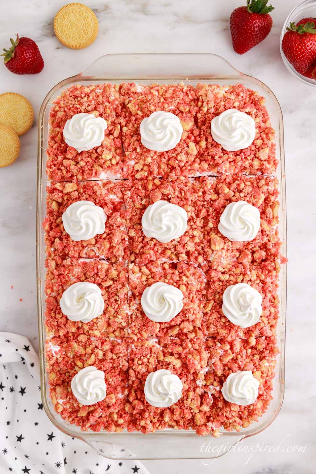 strawberry crunch poke cake sliced into 12 even pieces with a swirl of whipped cream on top of each section.