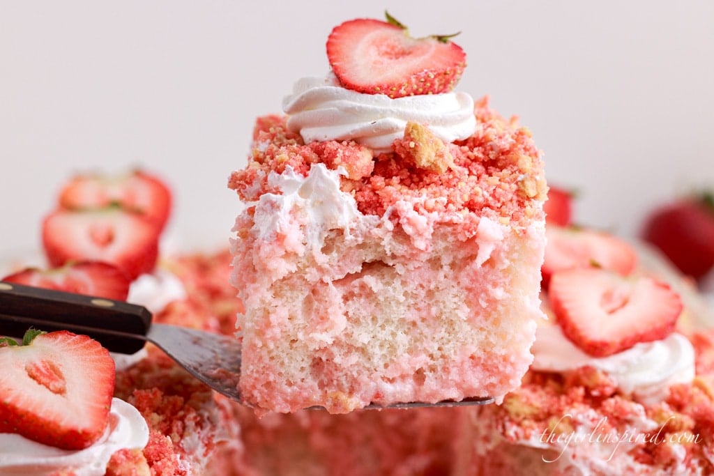 Single slice of strawberry crunch poke cake with the rest of the cake in the background