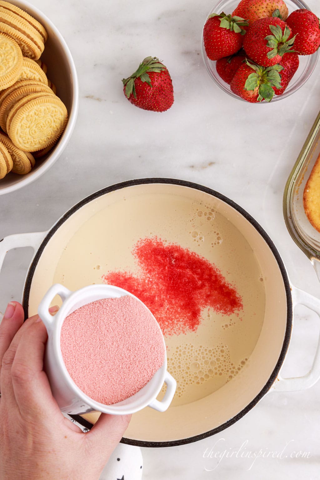 strawberry gelatin being sprinkled over the evaporated milk in a saucepan.