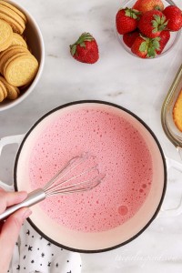 Milk and strawberry gelatin mixture whisked together atop a white marble surface with Oreos and strawberries in the tp corners and a polka dot cloth in the bottom corner