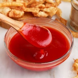 front view of the sweet and sour sauce served in a glass bowl with a wooden spoon coated with the sauce and some fries in the background