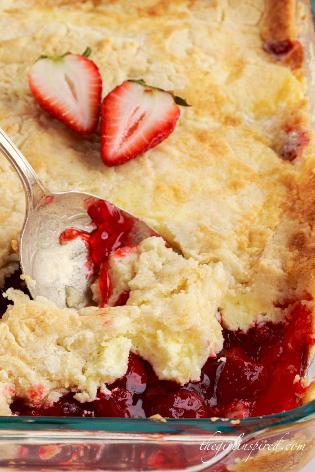 Strawberry cheesecake dump cake in a glass baking dish with serving spoon