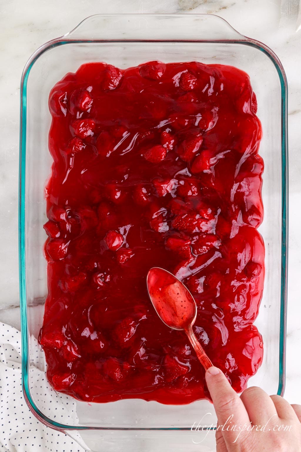 Strawberry pie filling spread into a baking dish, atop a white marble surface