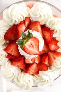 Dollops of whipped cream and fresh sliced strawberries added to the top of the trifle