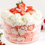Strawberry cheesecake trifle in a glass bowl atop a white marble surface with fresh strawberries in the background