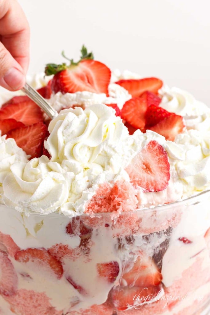 strawberry cheesecake trifle up close with a hand and spoon scooping a serving.