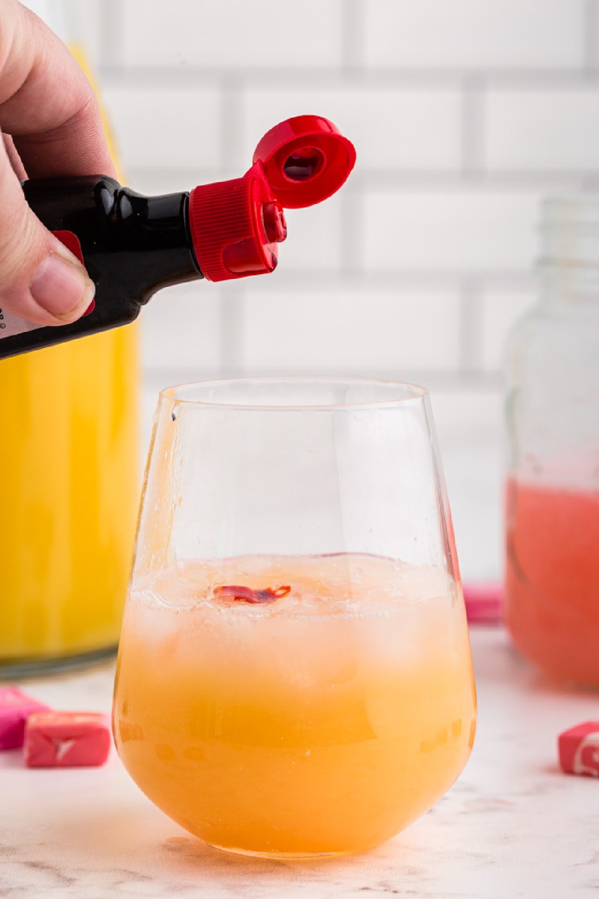 Adding a drop of red food coloring to starburst alcohol drink in stemless wine glass.