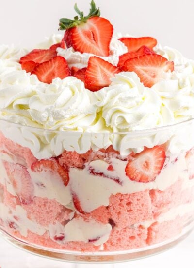Strawberry cheesecake trifle presented as layers of strawberry cake, whipped cream, and fresh strawberries in a glass trifle dish.