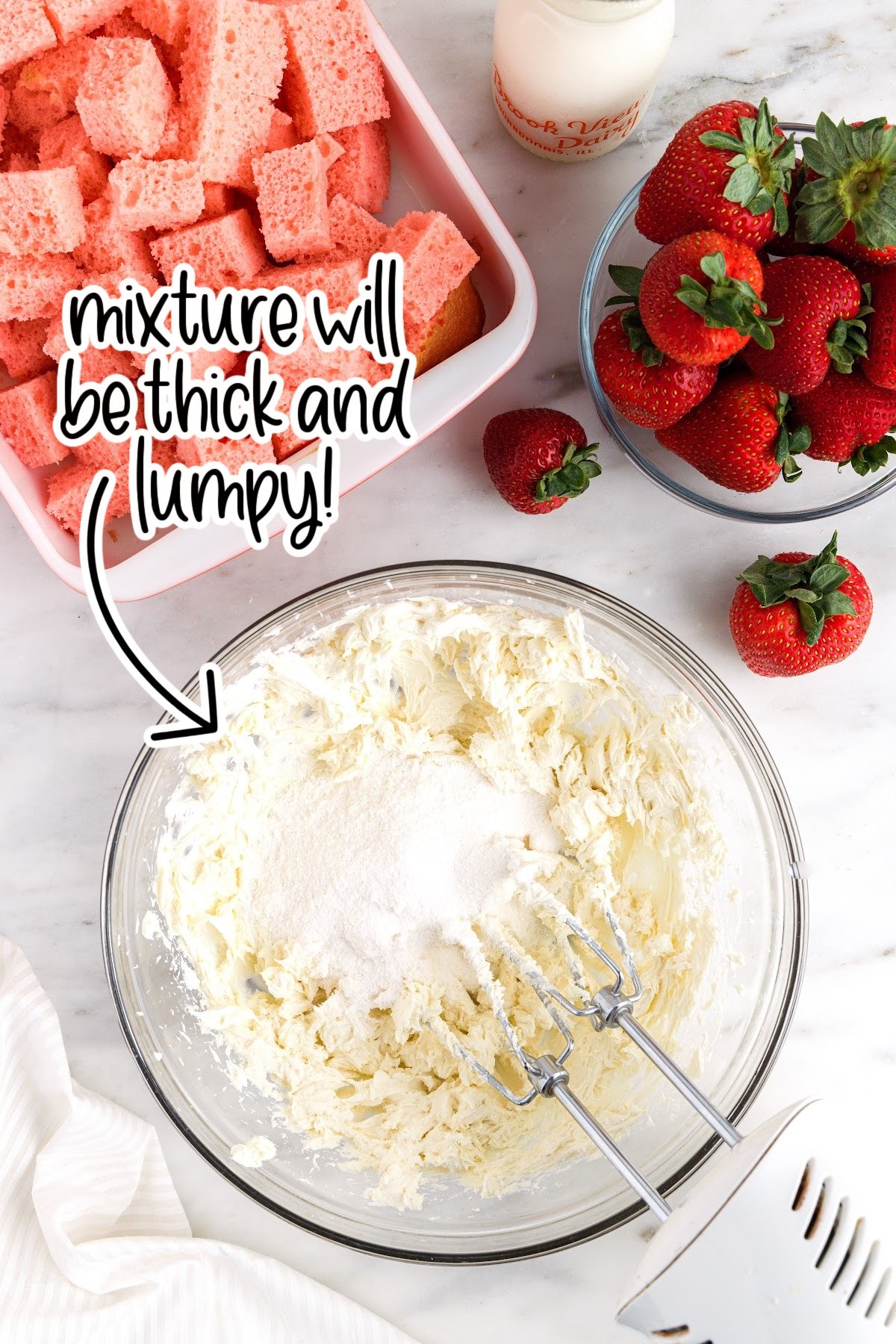 Blended cream cheese in glass mixing bowl with pudding powder added and text overlay "mixture will be thick and lumpy."