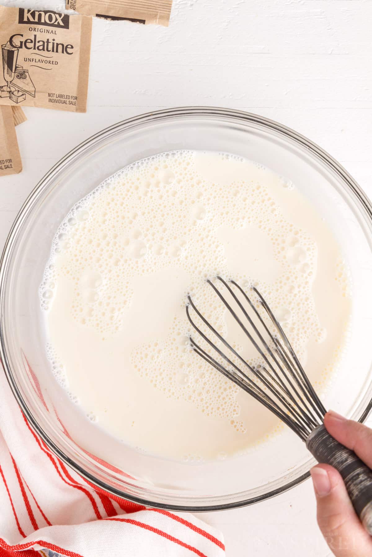 Whisking white gelatin mixture in glass bowl.