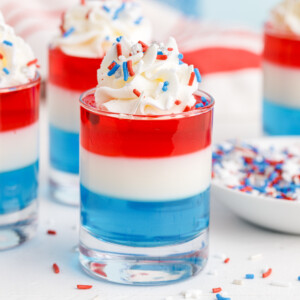 4th of July blue, white, and red layered jello in a shot glass topped with whipped cream and patriotic sprinkles.