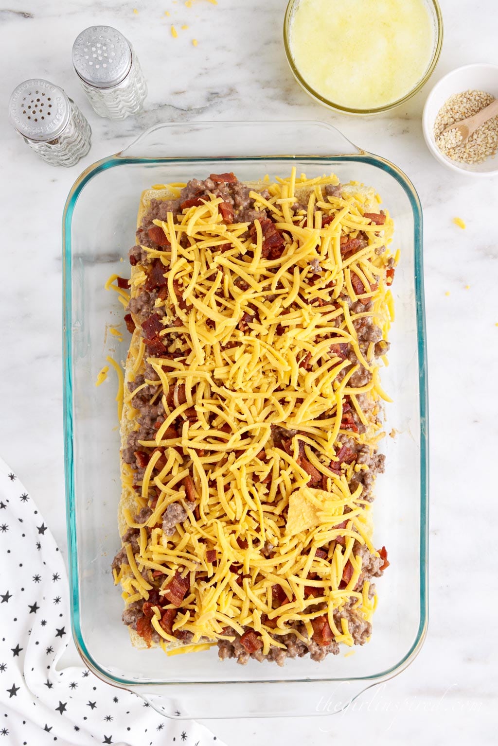 Halved rolls in baking tray topped with ground beef mixture and grated cheese, star linen, on a marble countertop