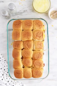Assembled bacon cheeseburger sliders in baking tray, star linen, on a marble surface