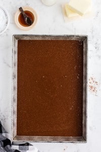 Raw cake batter poured into a prepared rectangular cake pan, butter and extract, black and white checked cloth, on top a white marble surface
