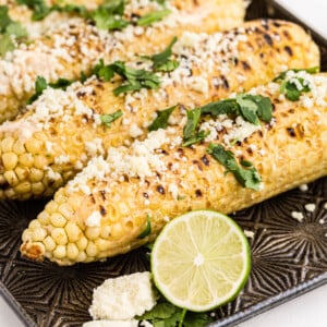 Grilled Mexican Street Corn with cilantro and crumbled cheese garnish, on baking sheet, limes on side