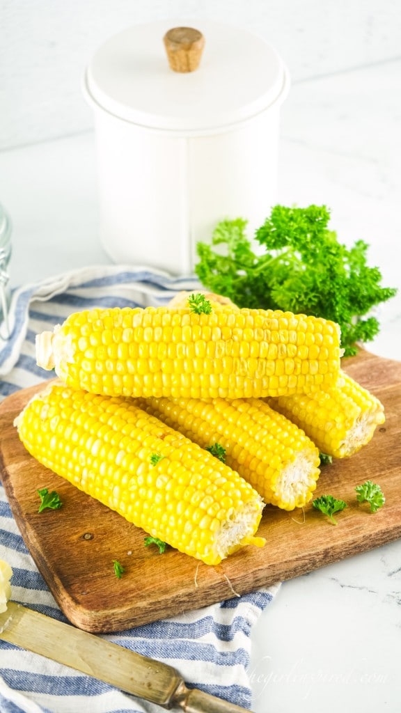 instant pot corn on the cob resting on a wooden cutting board next to garnish