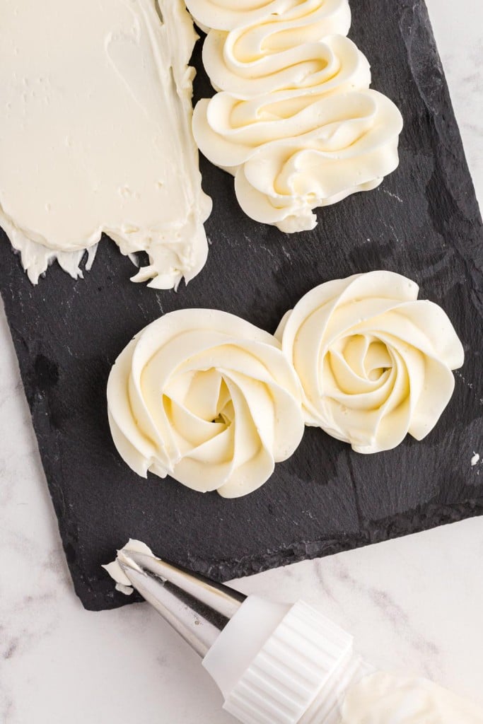 Black tray with piped Italian meringue buttercream, piping bag with nozzle, on a marble countertop