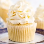 Italian meringue buttercream on a vanilla cupcake, atop a decorative side plate with additional frosted cupcakes in the background