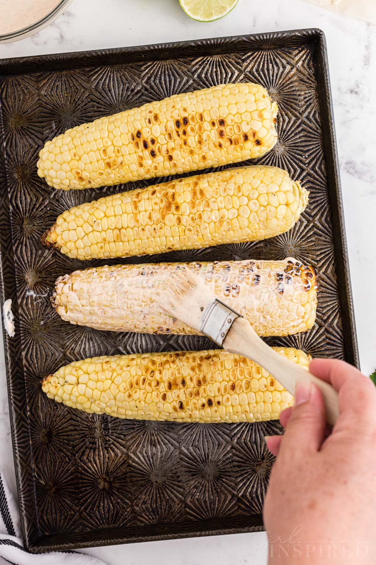 Pastry brush applying mayonnaise mixture to grilled Mexican street corn.