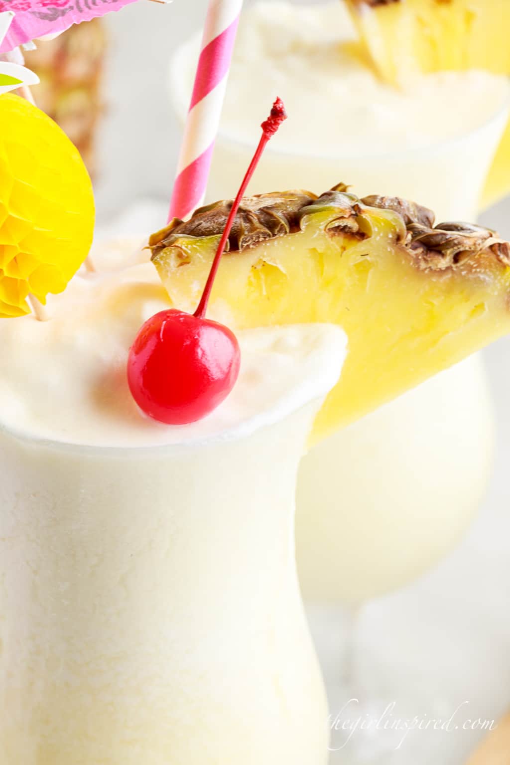 close up of a pina colada in a tall glass with a cherry and pineapple wedge
