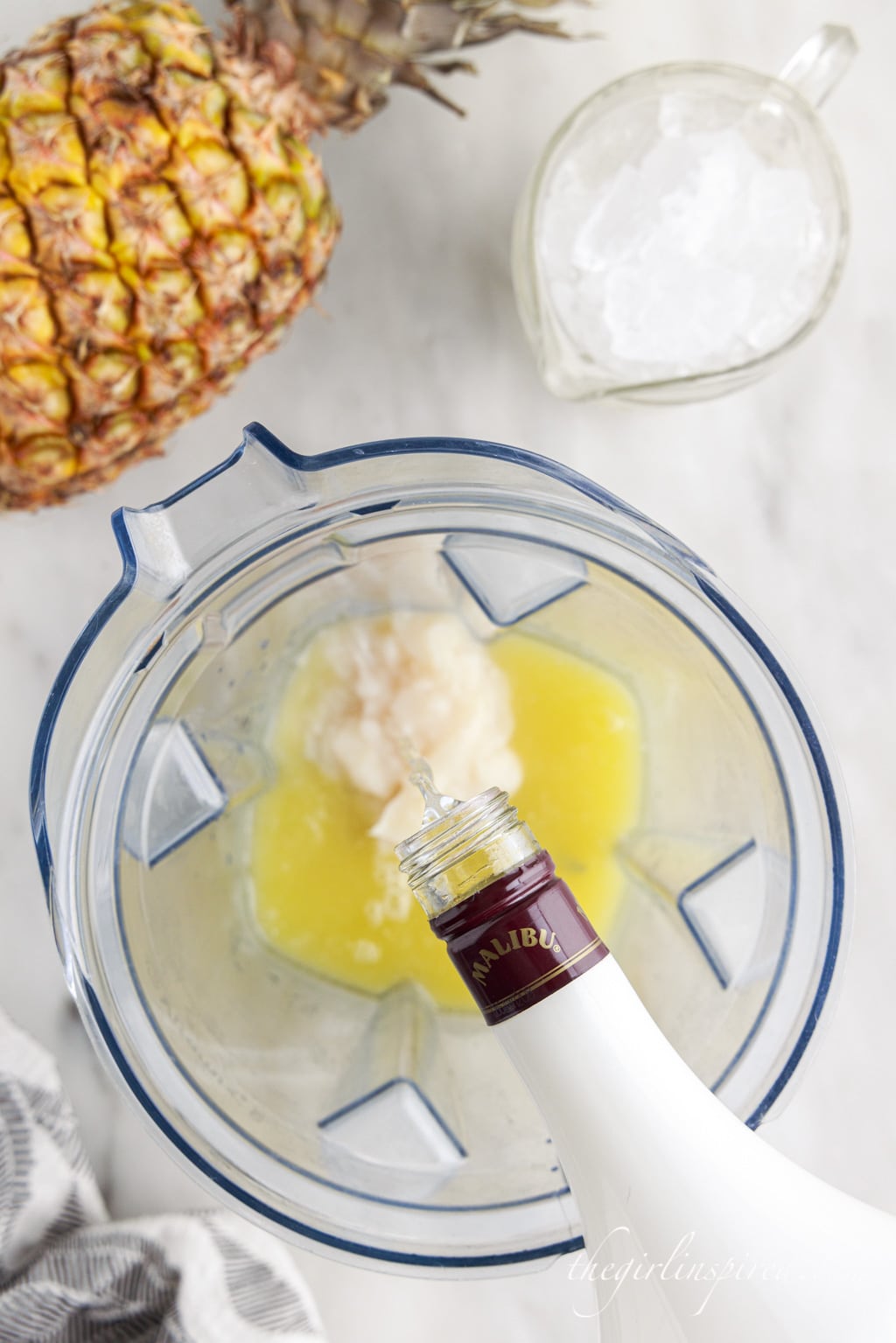 malibu rum pouring into blender filled with pineapple juice and cream of coconut.