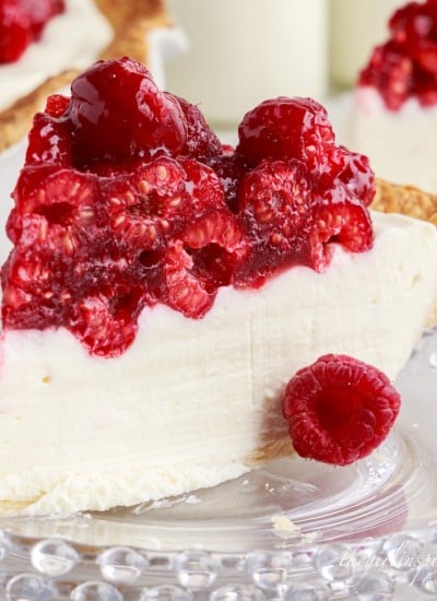 a slice of raspberry cream cheese pie on a glass plate with the rest of the pie in the background