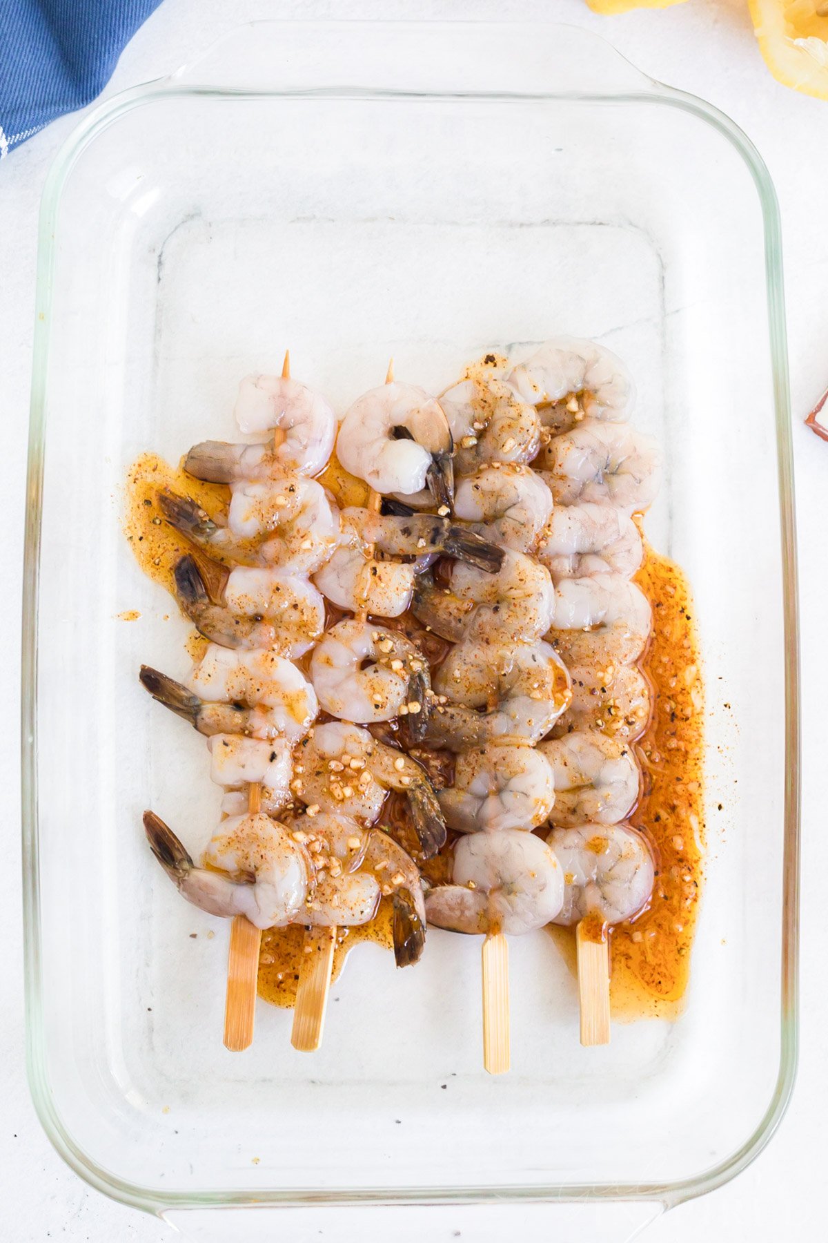 Shrimp skewers with marinade sauce drizzled over them, in a glass casserole dish.