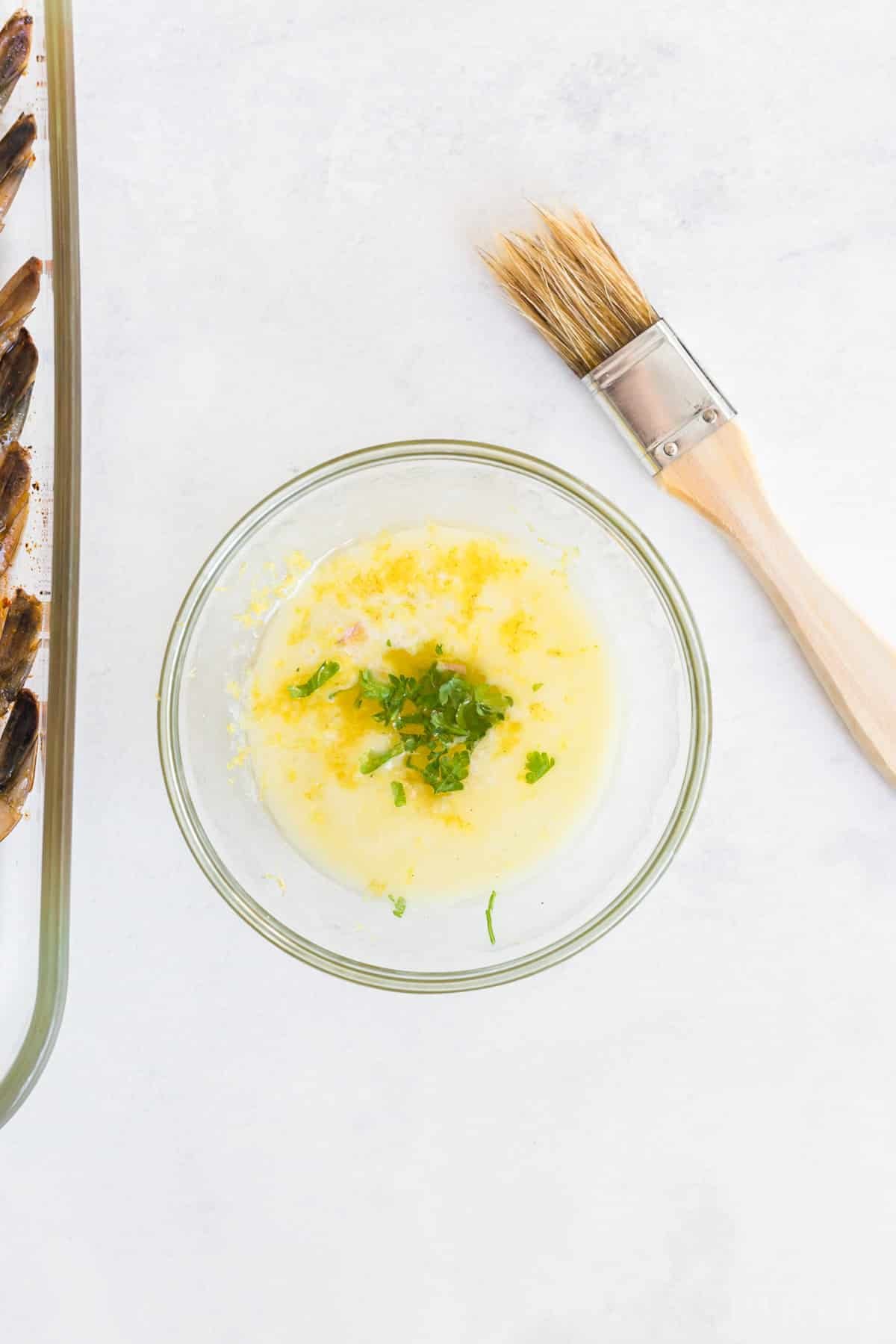 Melted butter, lemon zest, and parsley in a small glass bowl, with basting brush.