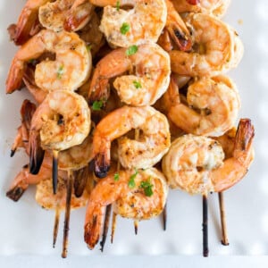 Grilled shrimp skewers stacked on a white platter with parsley garnish.