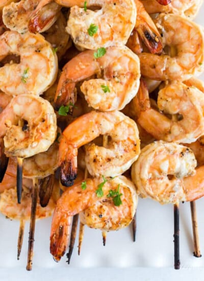 Grilled shrimp skewers stacked on a white platter with parsley garnish.