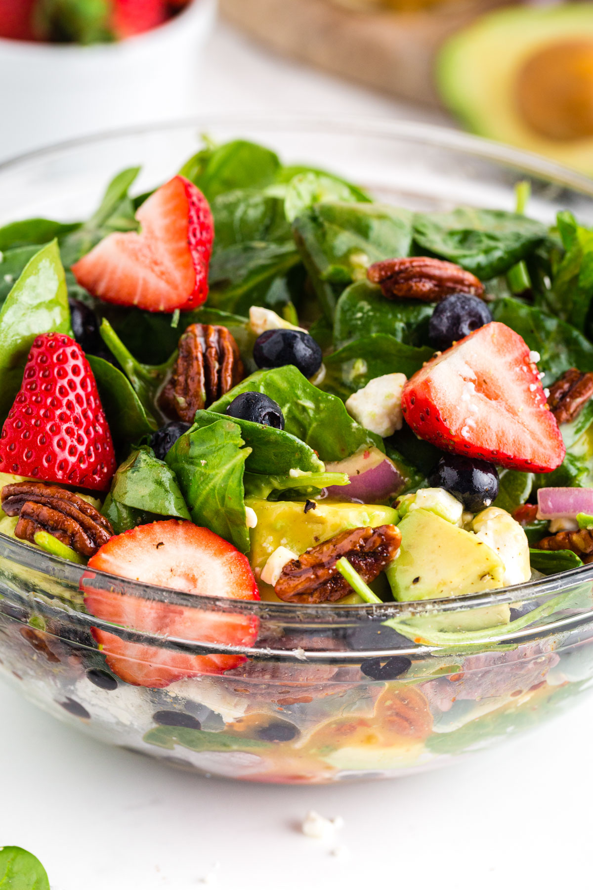 Strawberries, feta cheese, candied pecans, spinach, and avocado piled high in glass serving bowl.